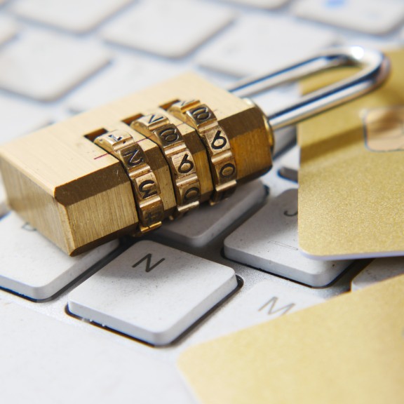 A white keyboard with a handheld combination gold lock and two gold stock credit/debit cards on top.